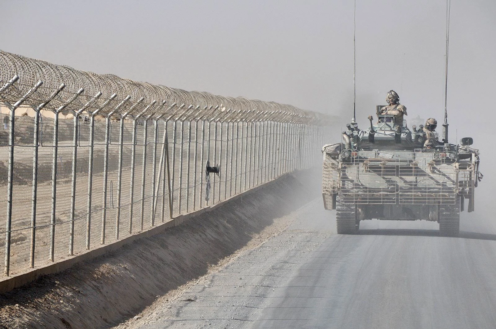Armoured vehicle fitted with cage armour beside a perimeter fence